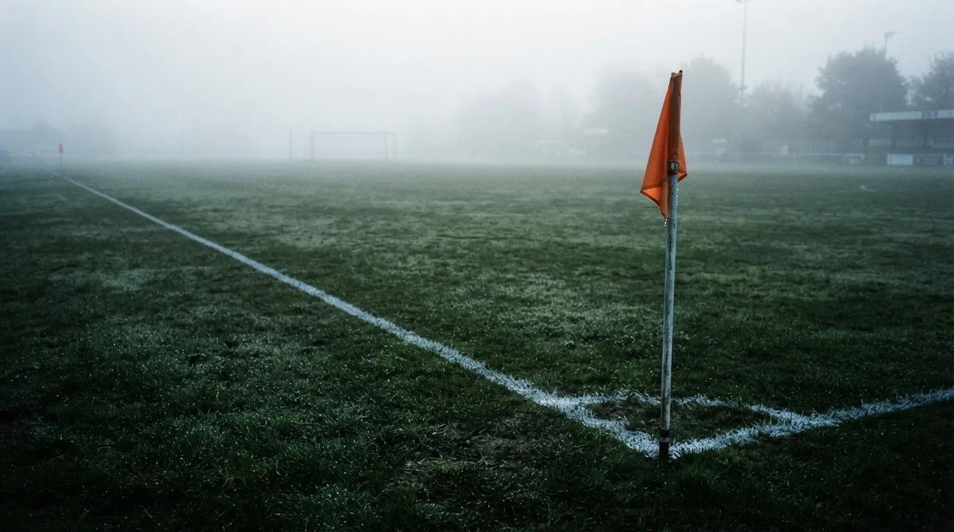 Der Rand eines Spielfelds mit weißer Linie und Eckfahne bei Nebel am frühen Morgen, ohne Menschen.