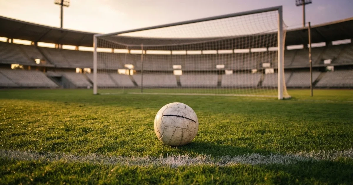Ein Fußball liegt im Strafraum direkt vor dem Tor mit Netz, im Hintergrund leere Ränge bei Dämmerung.