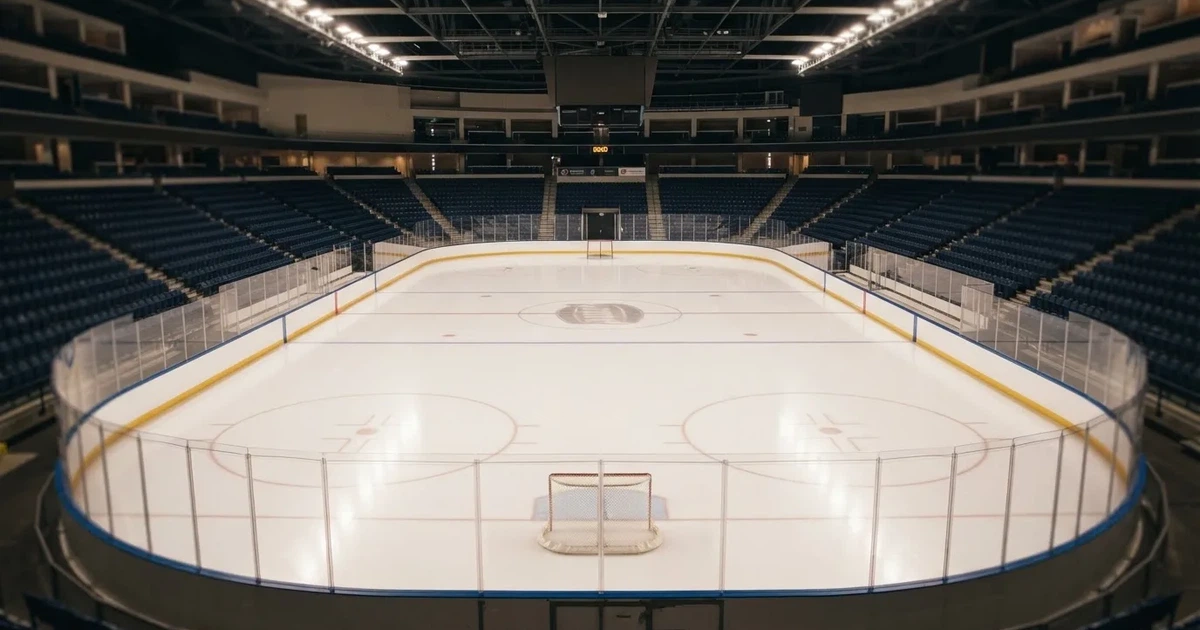 Eine Eishockeyhalle von der Tribüne aus gesehen, spiegelglatte Eisfläche, Banden ohne Schriftzüge, helles Flutlicht.