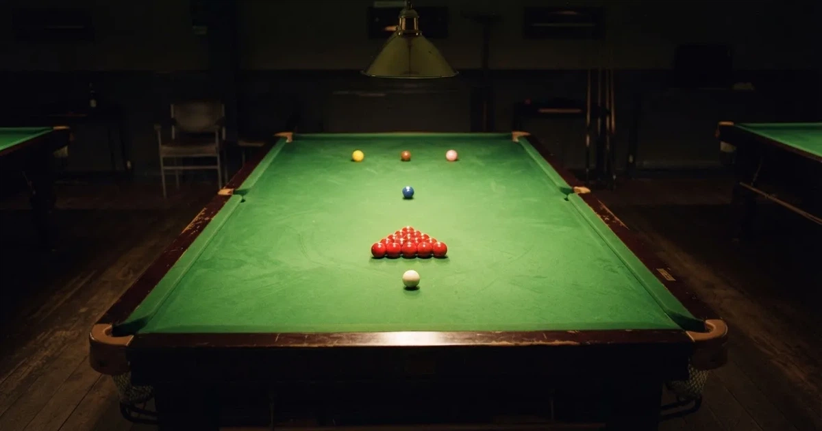 Ein Snookertisch mit grünem Tuch und aufgebauten roten Kugeln in einem abgedunkelten Raum unter einer hängenden Lampe.