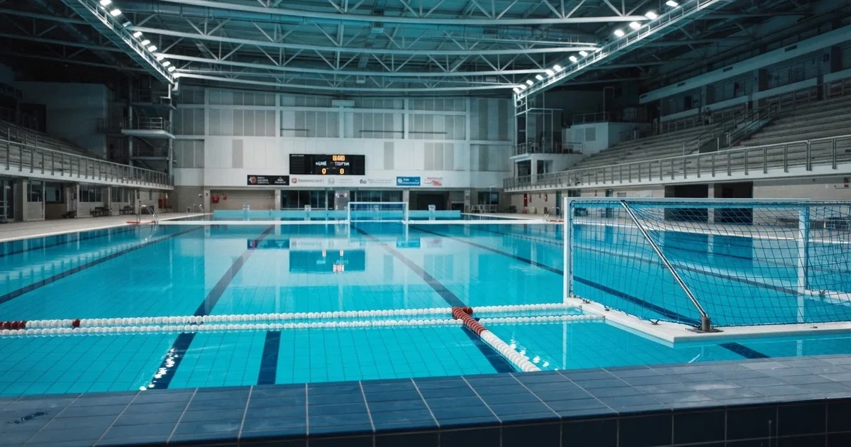 Ein Schwimmbecken mit türkisfarbenem Wasser und zwei schwimmenden Torrahmen am gegenüberliegenden Beckenrand, menschenleer unter Hallenlicht.